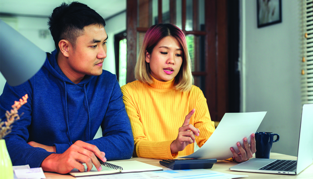 An Asian man and woman sit next to each other at a dining table and examine a document.