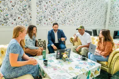 Multi-racial group of men and women sitting on couches with their laptops around a large coffee table in a Graduate Hotel lobby.