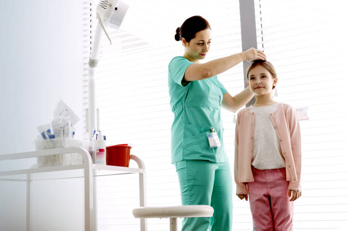Female Intermountain caregiver wearing scrubs measures the height of a young girl.