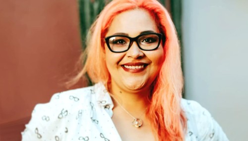Smiling Hispanic female with dyed pink hair and dark rimmed glasses
