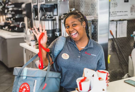 Closeup of a black female Chick-fil-A® Team Member smiling and showing off a to-go food bag with two to-go drinks secured in a drink holder.