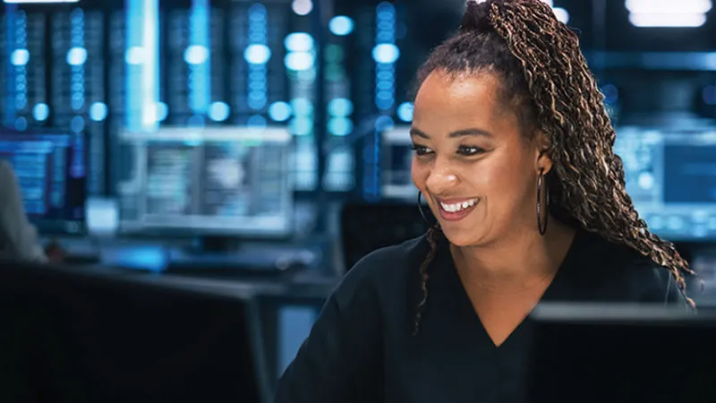 Black woman smiling and using a desktop computer in a data center.