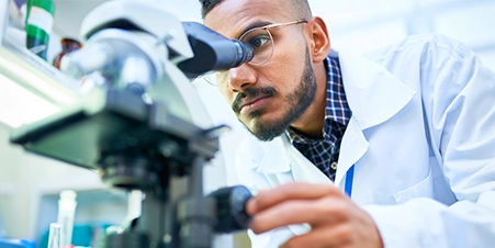 Indian male lab technician looking into a microscope.