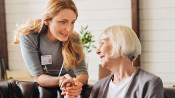 White female healthcare social worker tending to an elderly white female patient in a sitting room