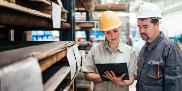 Black male operations manager wearing a hard hat and safety glasses working on a tablet in a warehouse