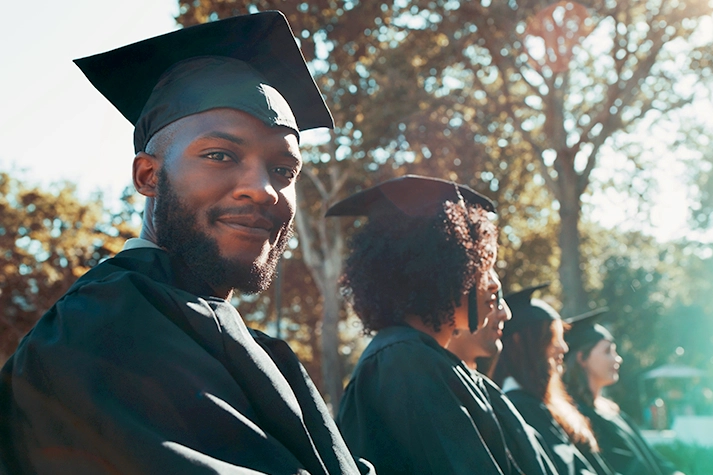Black male graduate in a cap and gown waiting to receive his degree