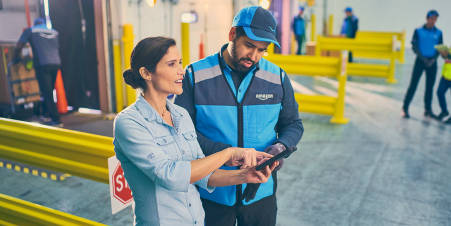 A female DSP showing something to a DA on a tablet and focusing on something off camera in the distribution center.