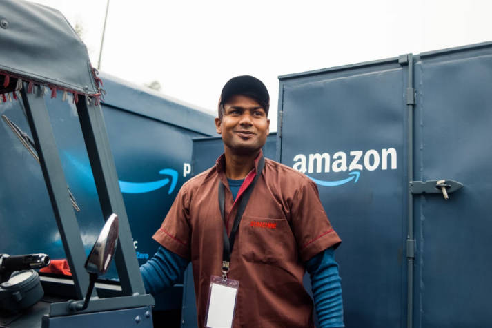 South Asian DSP owner standing between several Amazon delivery vans, smiling and looking beyond the camera.