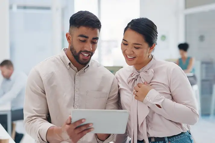 Hispanic male and Asian female coworkers looking at a tablet.