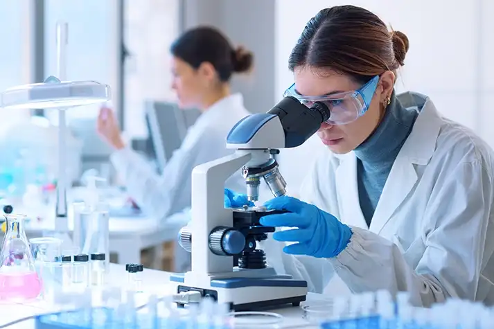 White female lab technician looking into a microscope.