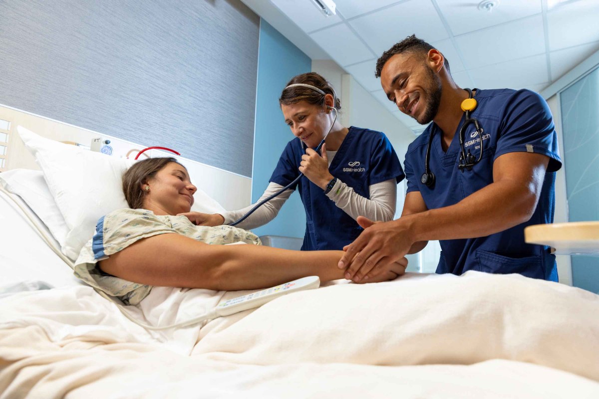 Black male and white female nurses tending to a white female patient in a hospital room