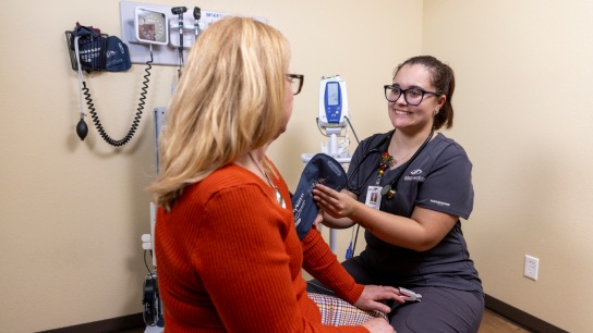 White female medical assistant taking a blood pressure reading on an older white female patient in an exam room