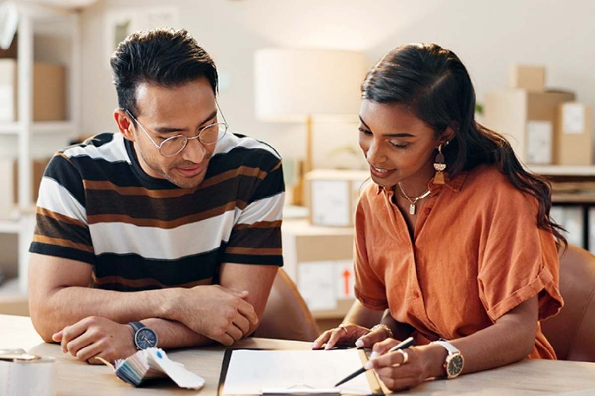 A man and woman sit at a table and look at information on a clipboard.