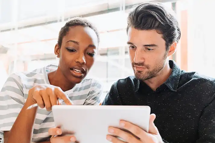 Black female and white male Prime employees sitting next to each other looking at information on a tablet.