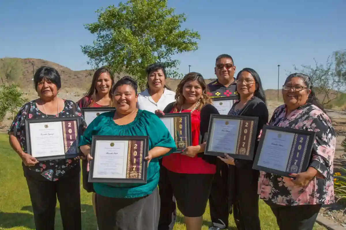 A group of seven female and one male members of the Gila River Indian Community posing outside with their ASU diplomas