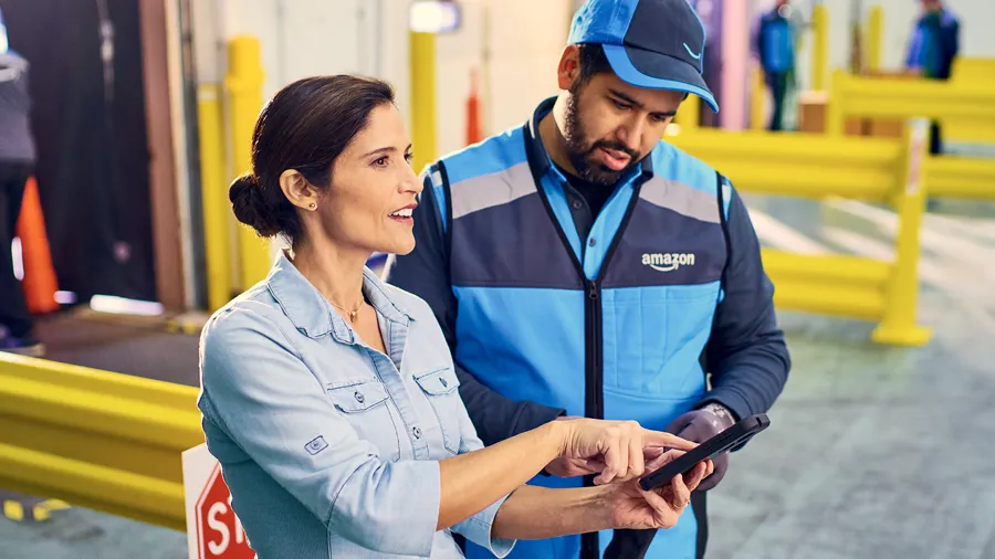 White female manager talking to a Hispanic male employee in uniform in a warehouse, pointing to a tablet screen